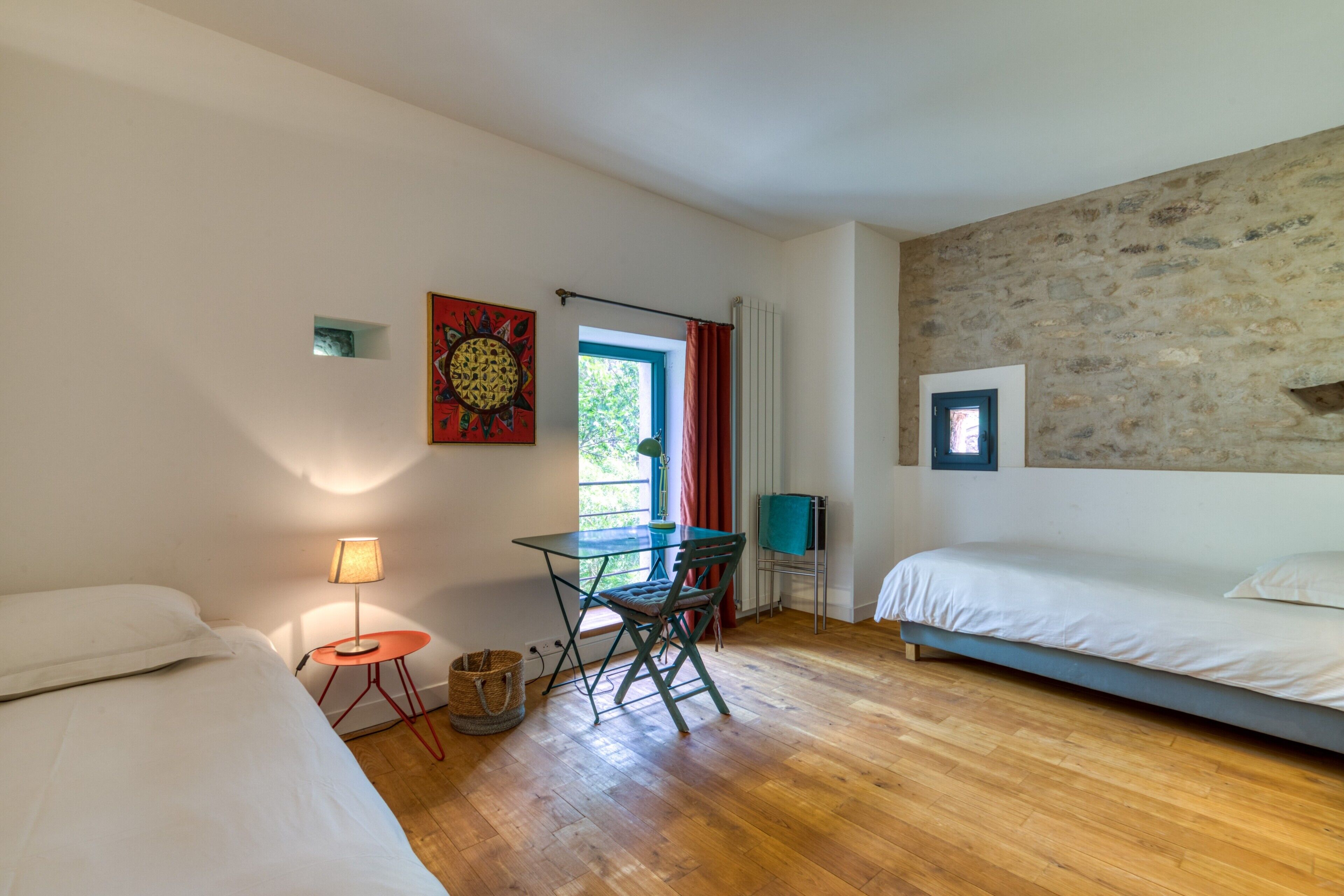 Una habitación con una cama, un escritorio con silla, una lámpara y un ventanal con cortinas.