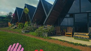 Une rangée de bâtiments modernes, dotés de toits triangulaires, d’une base en pierre et de détails en bois, entourés de jardins bien entretenus et sous un ciel dégagé.