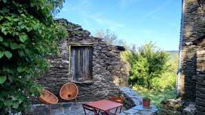 Un edificio de piedra con una ventana, una mesa con sillas y un camino de piedra.
