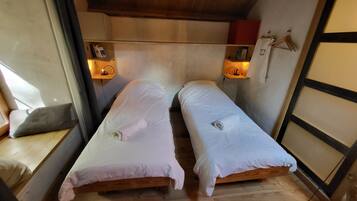 Een knus, compacte kamer met twee eenpersoonsbedden, een houten bankje en een klein plankje met een lamp.