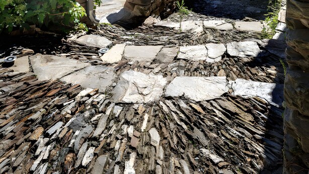 Un patio de piedra con un banco rústico de piedra, una mesita y un farol.
