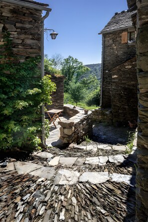 Un patio de piedra con un banco rústico de piedra, una mesita y un farol.