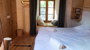 Una habitación con techo de madera, cama con ropa de cama blanca, ventana con cortinas y un armario de madera.