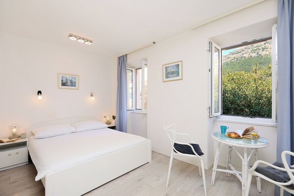 Une chambre à coucher comprenant un lit, des tables de chevet, une chaise, une petite table avec un livre et un verre, et une fenêtre donnant sur un paysage verdoyant.