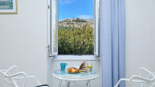 A room with a view of a hill, a table with a book, a glass of juice, and two chairs. - Sophie 1 - Old Town Heritage Suite (Dubrovnik)