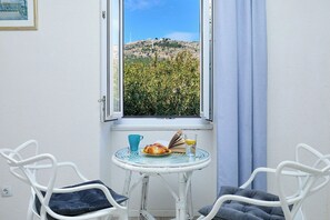 Une pièce avec vue sur une colline, une table avec un livre, un verre de jus de fruits et deux chaises.