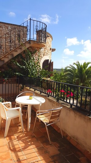 A terrace with a stone wall, a spiral staircase, a round table with chairs, and a railing with flowers. - Holiday Home 'Es Rafal Nou' with Private Pool, Wi-Fi and Air Conditioning (Santanyí)