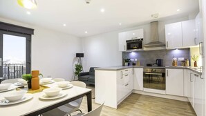 A modern kitchen with white cabinets, a built-in oven, and a dining area with a table set for four. - Student Only The Bridge Phase II (Newcastle-upon-Tyne)
