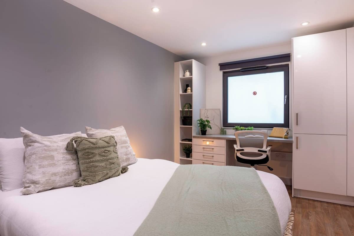 A bedroom with a bed, a desk, a chair, and a wardrobe.