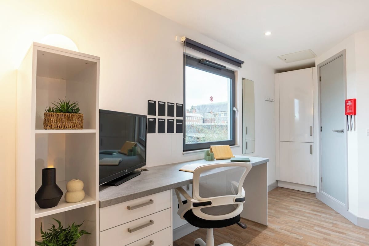 A modern office space with a desk, chair, shelving, and a window with a city view.
