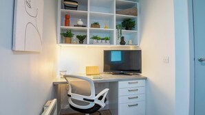 A modern office space with a desk, chair, TV, and shelves with plants and books. - Student Only The Bridge Phase II (Newcastle-upon-Tyne)
