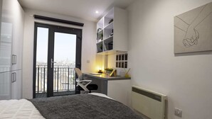 A bedroom with a bed, a desk, a chair, a radiator, and a balcony with a view. - Student Only The Bridge Phase II (Newcastle-upon-Tyne)