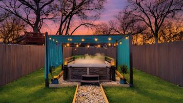 A hot tub with a stone surround, a wooden deck, and a string of lights.