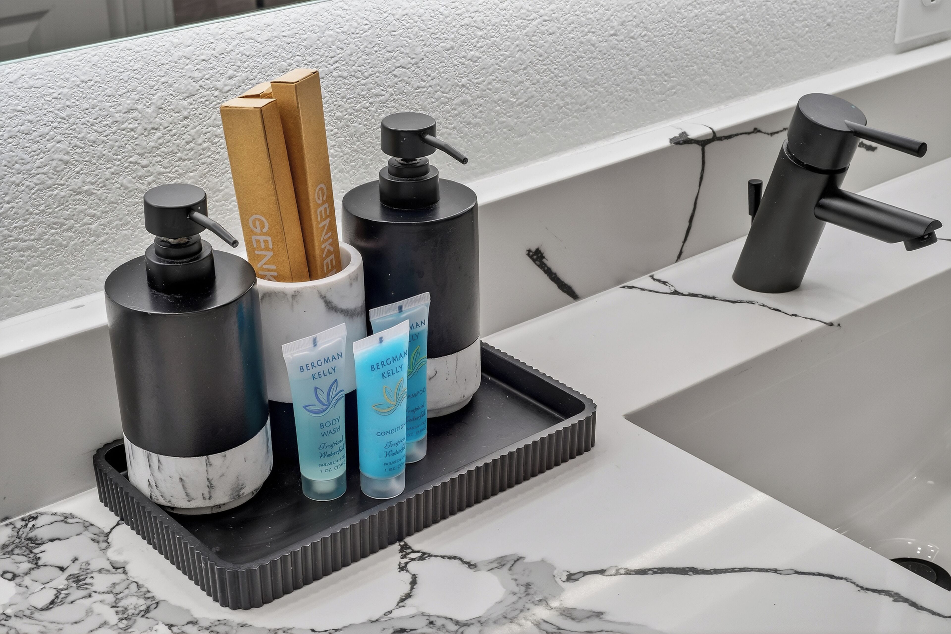 Een badkamermeubel met een wastafel, zwarte en witte marmertegels, een zwarte kraan en toiletartikelen, waaronder shampoo en conditioner van Bergman Kelly.