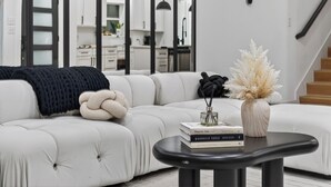 Ein modernes Wohnzimmer mit einem weißen Modulsessel, einem schwarzen Couchtisch und einer Vase mit Trockenblumen.