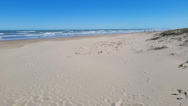 Ein weiter Sandstrand mit sanften Wellen und blauem Himmel.