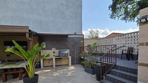 Un espace patio doté d’un sol en pierre, d’une table en bois, d’une plante en pot, d’un escalier et d’un coin salon agrémenté d’une rambarde.
