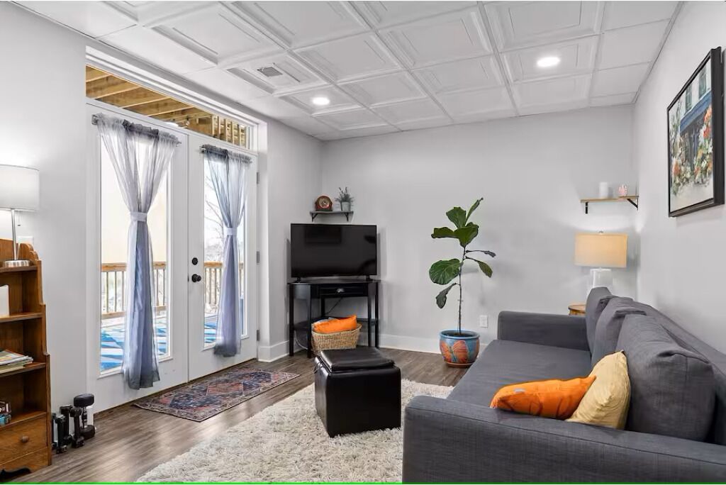 A living room with a grey sofa, a television, a potted plant, and a bookshelf.