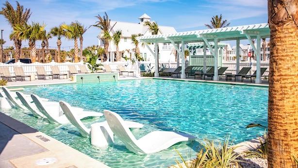 A swimming pool with lounge chairs, palm trees, and a covered seating area. - Sol Seekers 109 PLA (Port Aransas)