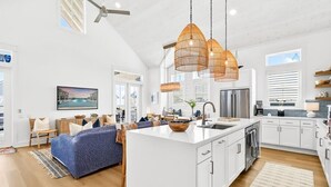 A spacious kitchen with a large island, white cabinetry, and a hanging rattan light fixture. - Sol Seekers 109 PLA (Port Aransas)