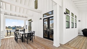 A covered outdoor patio with a wooden deck, a table with chairs, and a view of houses in the background. - Sol Seekers 109 PLA (Port Aransas)