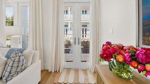 Una sala de estar con un sofá, una mesa de centro con un florero y una puerta que da a un balcón exterior, con vistas a edificios.