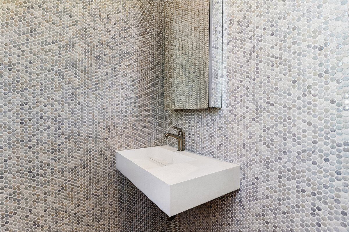 Une salle de bain avec un lavabo blanc, un miroir et un mur recouvert de carreaux.