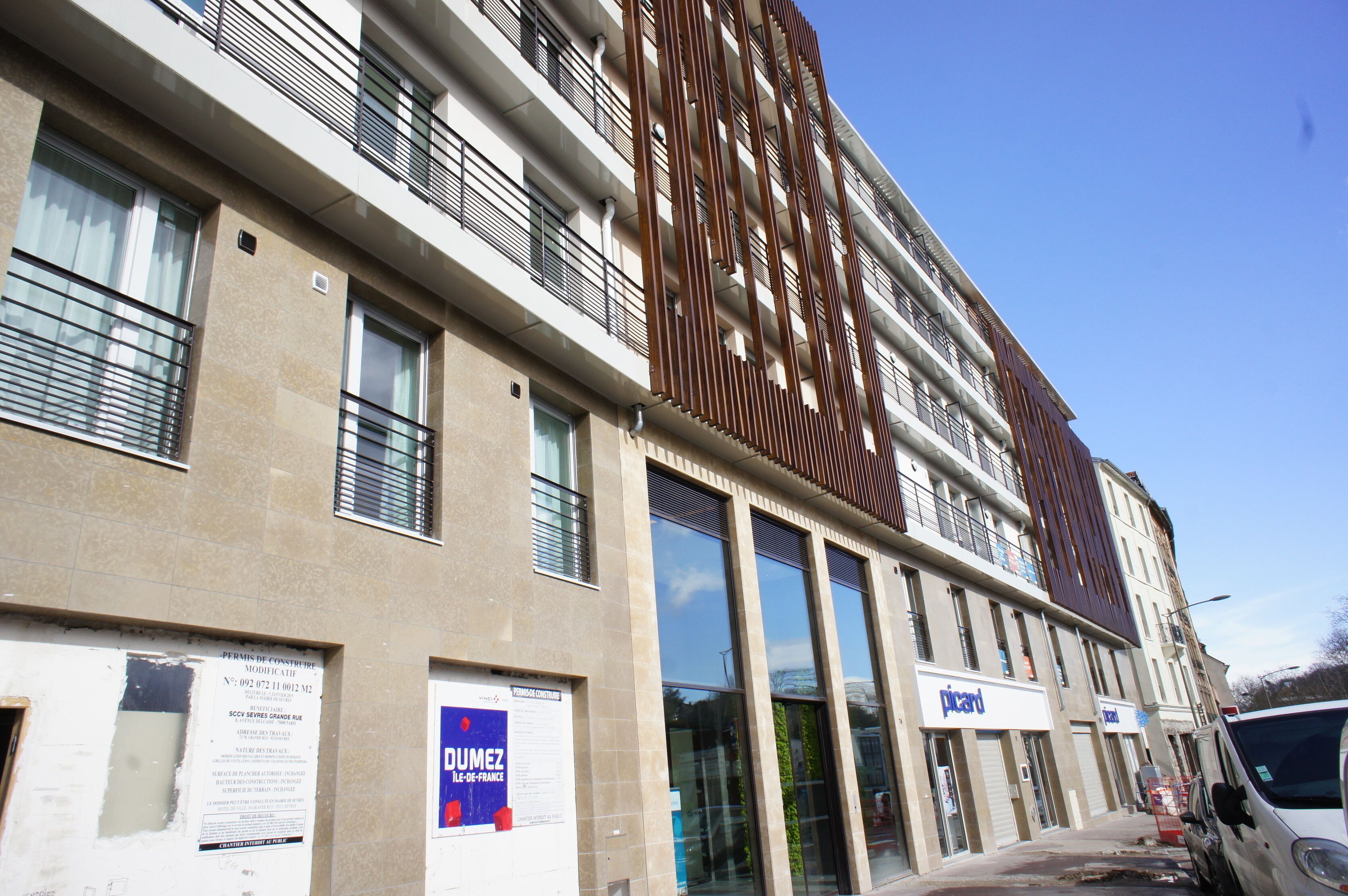 Un edificio de varios pisos con amplios ventanales, un llamativo diseño de paneles verticales de madera y un escaparate con letrero.