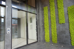 A modern interior with a glass door entrance, a wall-mounted green plant feature, and a tiled floor. - Zenao Appart'hôtels Sèvres (Sèvres)