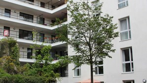 En flervåningsbostadsbyggnad med balkonger, ett träd på innergården och en liten trädgårdsyta.