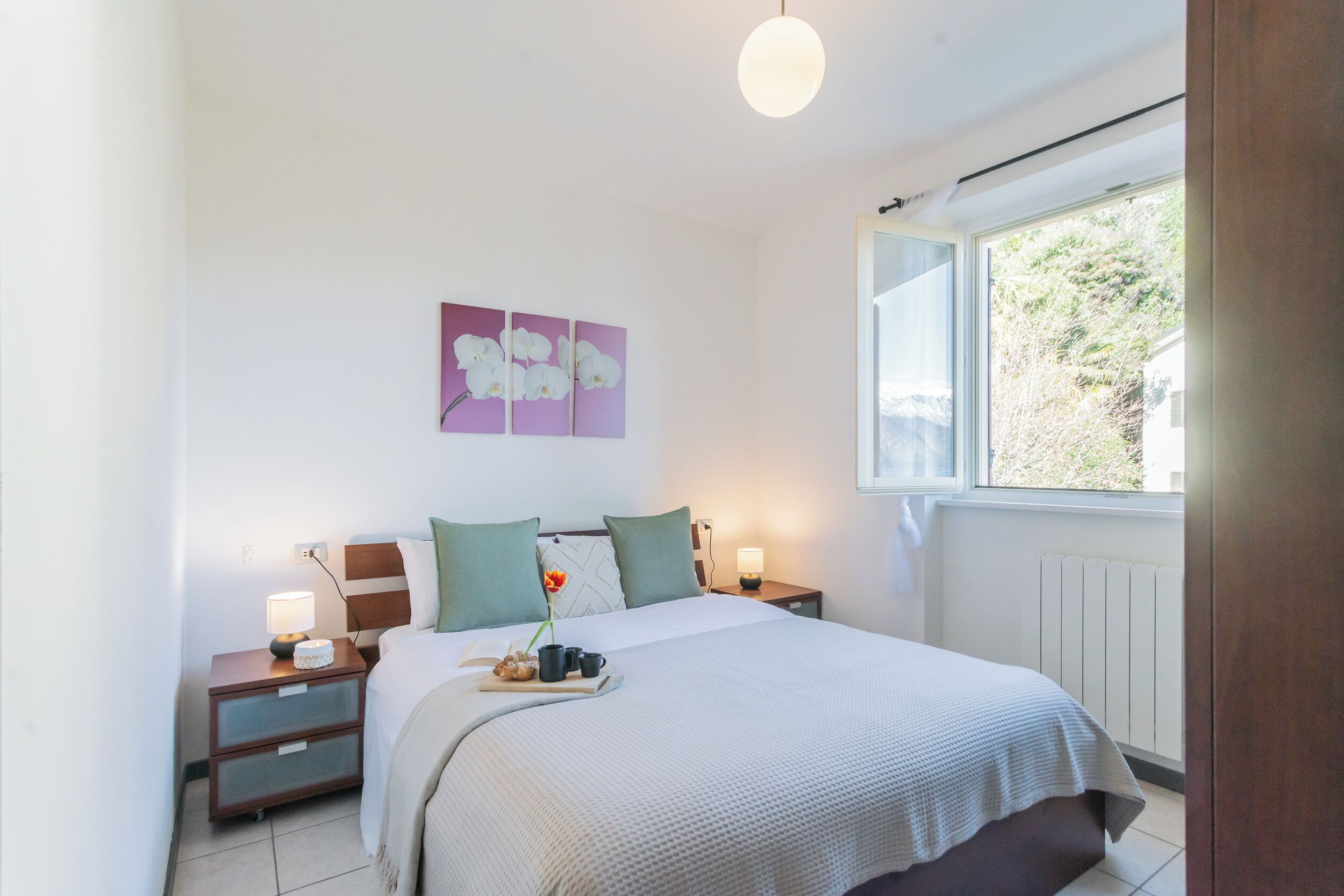 A bedroom with a bed, bedside tables, a window, and a wall-mounted artwork.