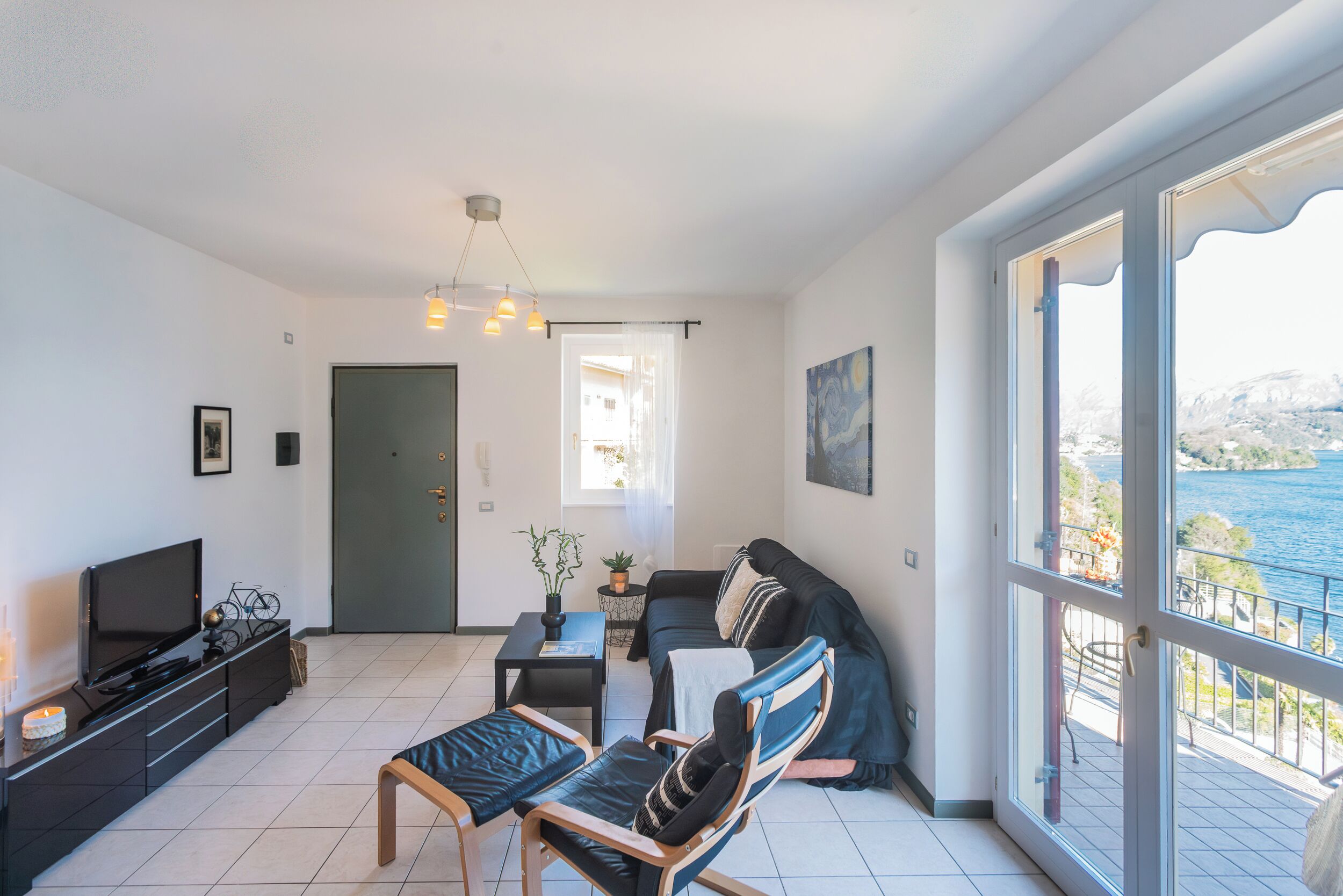 Un soggiorno moderno con televisione, divano, poltrone e un balcone vista mare.