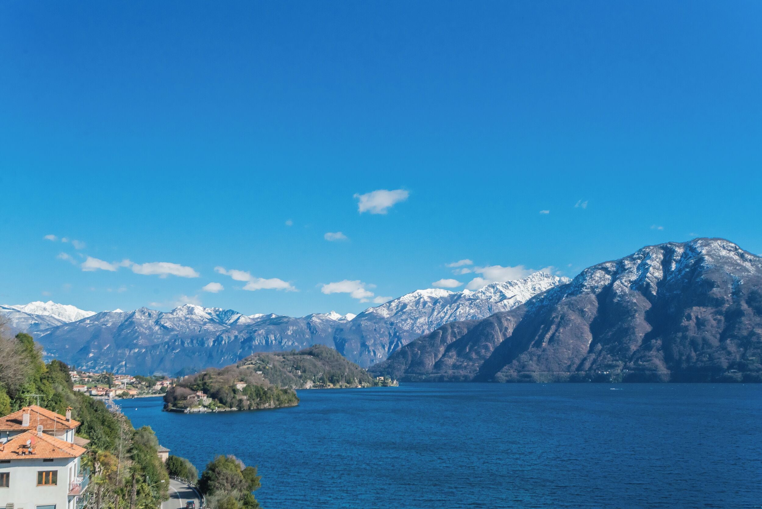 A lake with mountains in the background and a building with a red roof in the foreground.