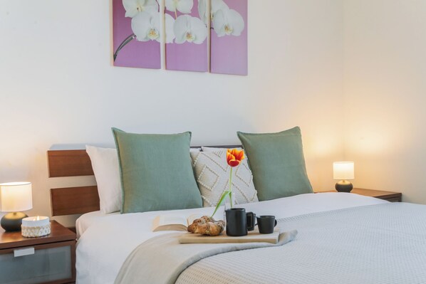 A neatly made bed with pillows, a bedside table with a lamp, a tray with a book, mug, and a flower. - Alba on Lake Como (Sala Comacina)