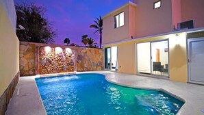 A swimming pool with a stone wall and a modern building in the background. - Poolside Retreat  Lounge Parking Near Downtown (La Paz)