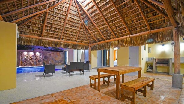 A thatched-roof structure with a tiled floor, a pool, and a dining area with benches. - Poolside Retreat  Lounge Parking Near Downtown (La Paz)