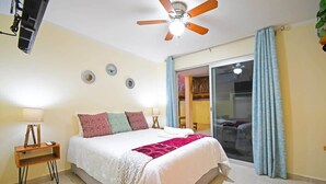 A bedroom with a bed, a ceiling fan, a nightstand, a lamp, and a sliding glass door to the outside. - Poolside Retreat  Lounge Parking Near Downtown (La Paz)