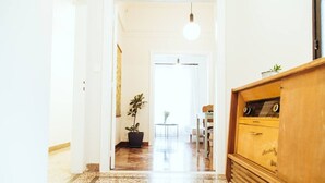 A hallway with a wooden cabinet, a potted plant, and a table with chairs. - we saw athens from 4b (Athina)