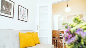 A living room with a sofa, yellow cushions, a dining area with a table and chairs, and a hanging light fixture. - we saw athens from 4b (Athina)