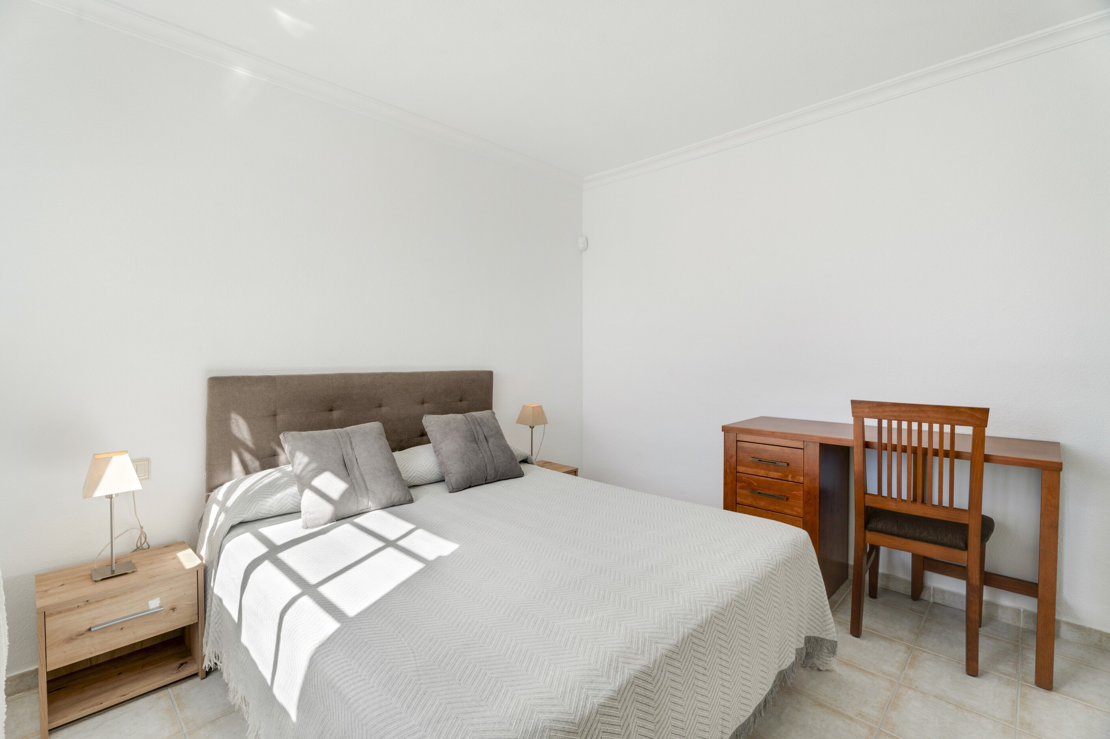 A bedroom with a bed, bedside tables, a desk, and a chair.