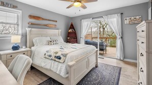 A bedroom with a bed, a ceiling fan, a bookshelf, a window with blinds, and a view of the outdoors. - Lakeside Pines: Waterfront > Bike in/out > Game Room > Fitness Room (Bella Vista)