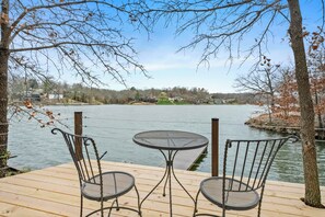 Une terrasse en bois avec deux chaises en métal et une table, donnant sur une étendue d’eau.