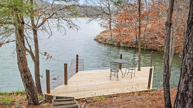 A wooden dock with a table and chairs, surrounded by trees and a body of water. - Lakeside Pines: Waterfront > Bike in/out > Game Room > Fitness Room (Bella Vista)