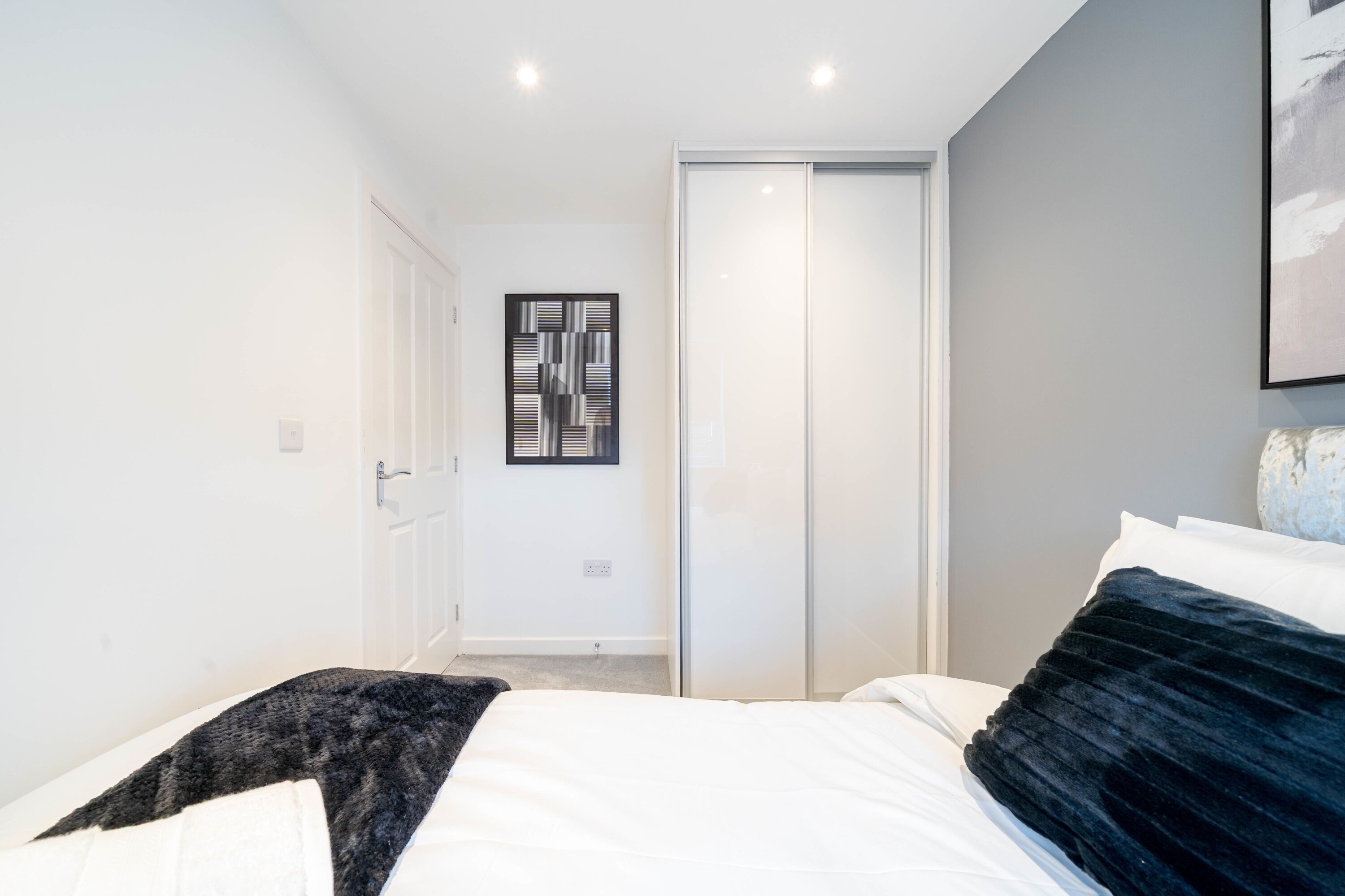Ein modernes Schlafzimmer mit einem Bett, einem Kleiderschrank und einem gerahmten Kunstwerk an der Wand.