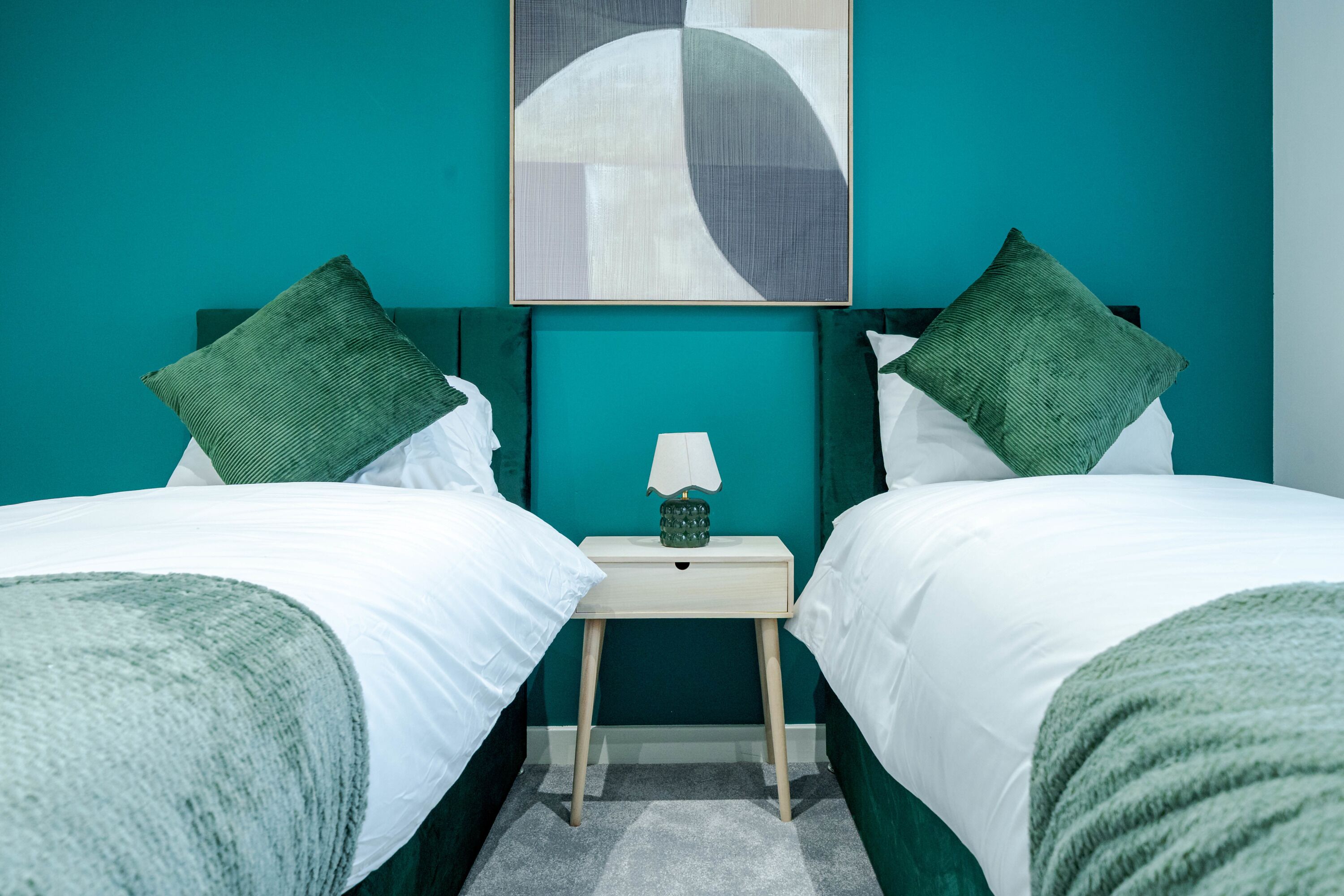 Une chambre avec deux lits, une table de chevet avec une lampe et un mur de couleur turquoise.