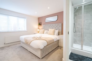 A modern bedroom with a large bed, a bedside table, a mirror, and a shower area. - Lytham St Annes FY8 | 3BR Home | Near Blackpool (Lancashire)