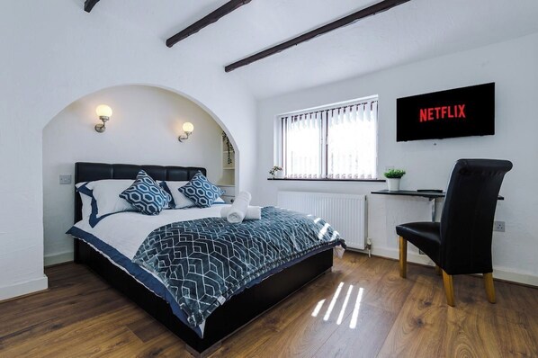 A bedroom with a bed, a desk, a chair, a TV, and a window.