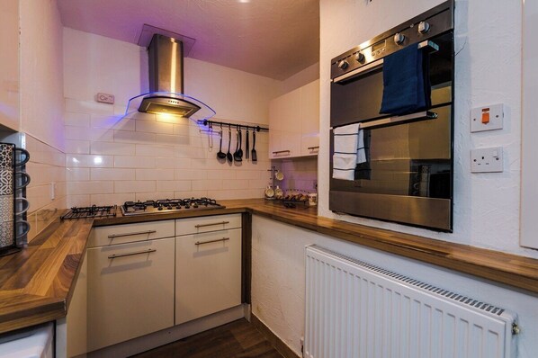 A modern kitchen with a gas stove, stainless steel oven, and white cabinetry.