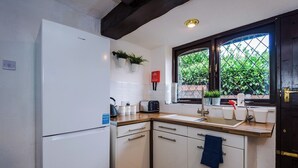 A compact kitchen with a white refrigerator, a wooden countertop, a sink, and a window with a view of greenery. - Spacious 4-Bed House | Near Wigan & Warrington (Golborne)