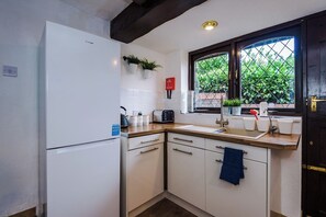 A compact kitchen with a white refrigerator, a wooden countertop, a sink, and a window with a view of greenery. - Spacious 4-Bed House | Near Wigan & Warrington (Golborne)